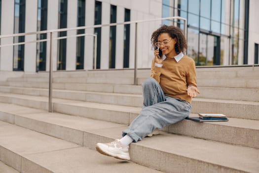 Smiling female freelancer talking phone with client while sitting on building background