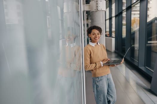 Smiling female entrepreneur using laptop while standing on office background and looks camera