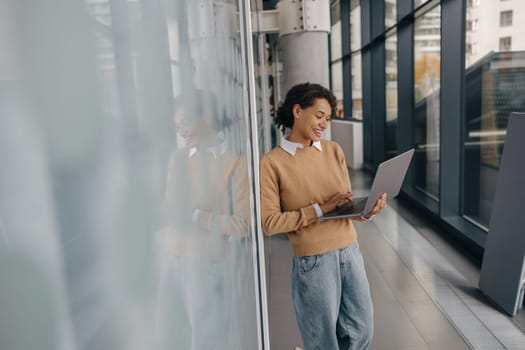 Pretty female freelancer working on laptop while standing on modern coworking background