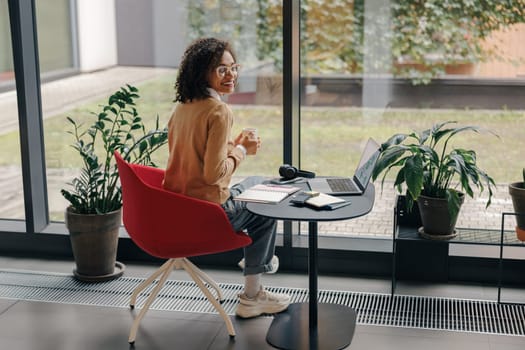 Smiling business woman in eyeglasses have a coffee break during working on laptop in cozy cafe