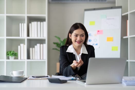 Beautiful asian businesswoman woman using calculator and laptop for doing finance on an office desk, tax, report, accounting, statistics, and analysis research concept.