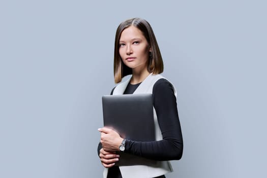 Portrait of young serious business fashionable woman with laptop in her hands on gray studio background. Work, study, business education technology concept