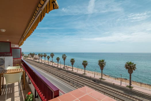 Embankment and ocean water view from hotel terrace in Vilassar de Mar. Picturesque sea waterfront with palms and railroad under blue sky