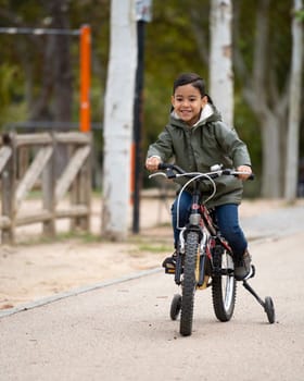 Portrait of happy boy riding a bicycle in a public park with copy space.