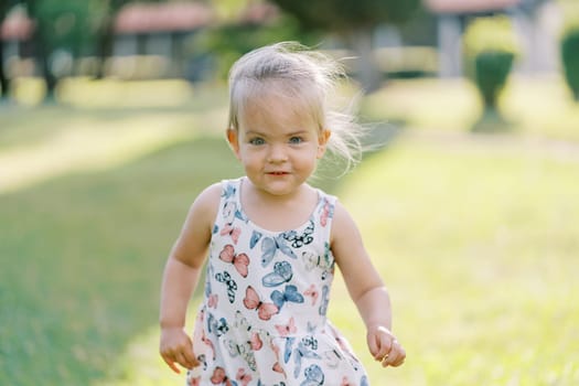 Little smiling girl with her hair fluttering in the wind stands on a green meadow. High quality photo