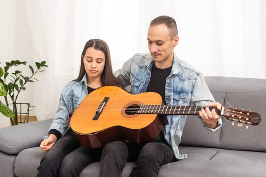 Father guy teaching girl teenager daughter guitar playing at home. Family musical lessons with strings instrument. High quality photo