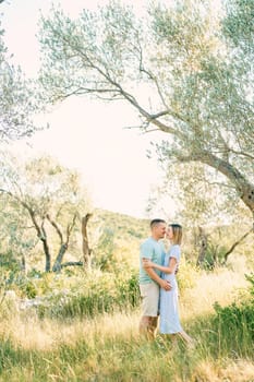 Smiling man and woman hugging with their noses touching while standing in a green park. High quality photo