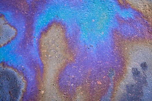 Spots of oil or gasoline are scattered randomly on the asphalt after rain. Abstract background close-up