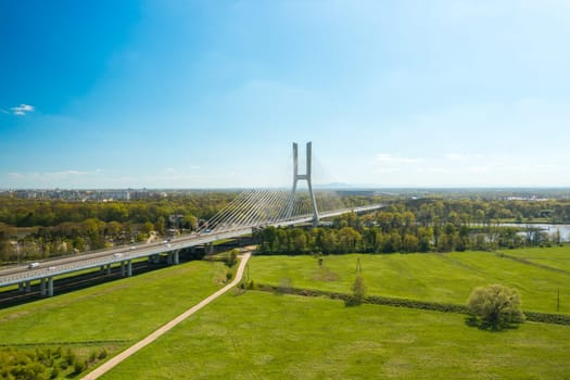 Pylon bridge with cars over green island on Oder river in Wroclaw. Cable-stayed Redzinski Bridge and scenic spring landscape aerial view