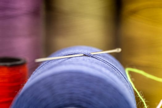 A closeup of a needle in a thread with other colorful needles in the blurry background