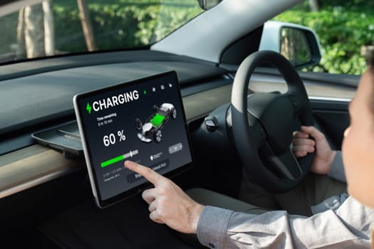 Electric car driver checks battery charging status, range and charging limit on app screen in the car. Smart technology device show EV car recharging data of electric storage in car battery innards.