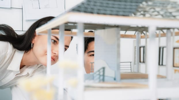 Close up of cooperative professional engineer working together to measuring house model structure. Young beautiful architect measure house model while male engineer support performance. Immaculate.