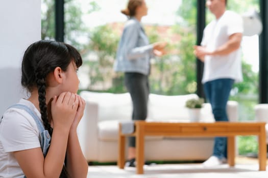 Stressed and unhappy young girl huddle in corner crying and sad while her parent arguing in background. Domestic violence at home and traumatic childhood develop to depression. Synchronos
