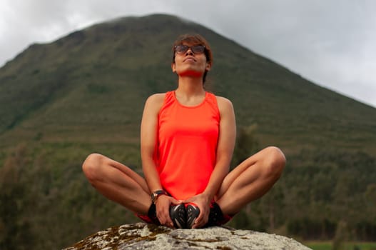 sporty woman in orange t-shirt sitting in yoga position looking towards the sky relaxing body and mind. . High quality photo