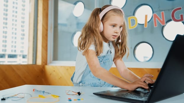 Young student working on laptop or studying in online classroom. Caucasian girl typing on laptop while doing homework or listening music.Little kid wearing headphone. Creative learning. Erudition.