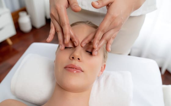 Closeup woman enjoying relaxing anti-stress head massage and pampering facial beauty skin recreation leisure in dayspa modern light ambient at luxury resort or hotel spa salon. Quiescent
