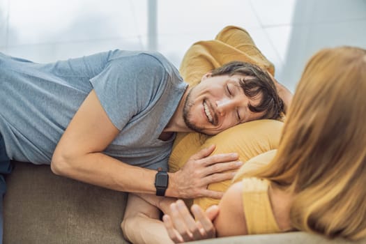 Tender moment as husband lovingly embraces his pregnant wife's belly while they lie together on the sofa, sharing warmth and anticipation.