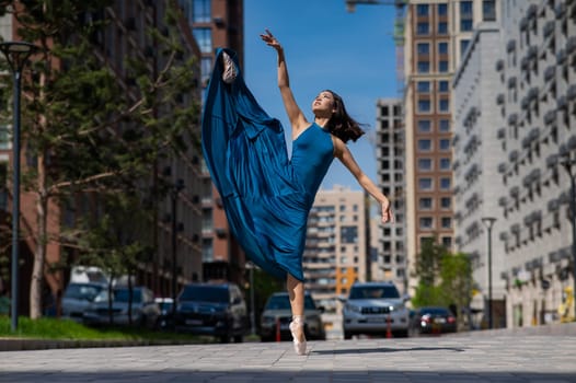 Beautiful Asian ballerina in blue dress posing in splits outdoors. Urban landscape