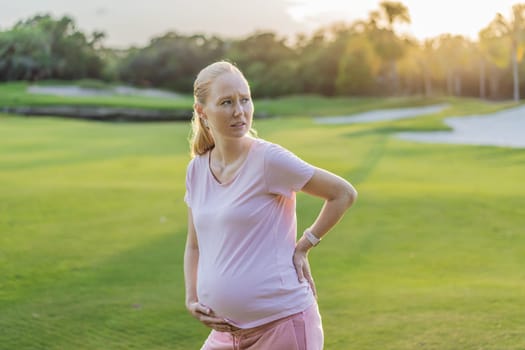 Expectant woman experiences back pain outdoors, seeking relief and comfort during pregnancy with a gentle outdoor stretch or rest.