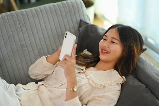 Relaxed young woman chatting in social networks on smart phone while lying on a sofa at home.