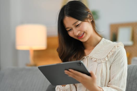Cheerful young woman using digital tablet on couch, surfing the net or shopping online.