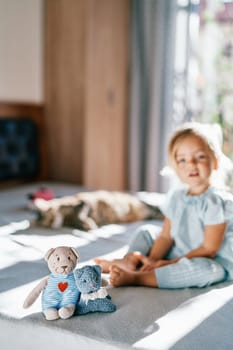 Teddy bear and a toy cat sit on the bed and hug against the background of a little girl. High quality photo