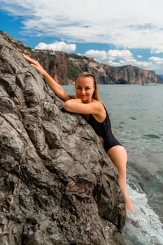 Woman swimsuit sea. Attractive blonde woman in a black swimsuit enjoying the sea air on the seashore around the rocks. Travel and vacation concept