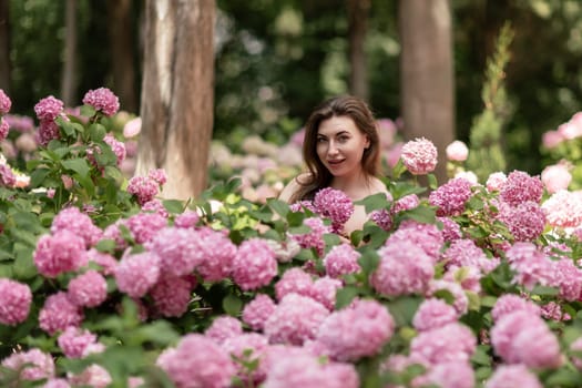 Hydrangeas Happy woman in pink dress amid hydrangeas. Large pink hydrangea caps surround woman. Sunny outdoor setting. Showcasing happy woman amid hydrangea bloom
