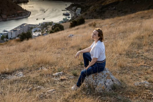 Happy woman on sunset in mountains. Woman siting with her back on the sunset in nature in summer. Silhouette