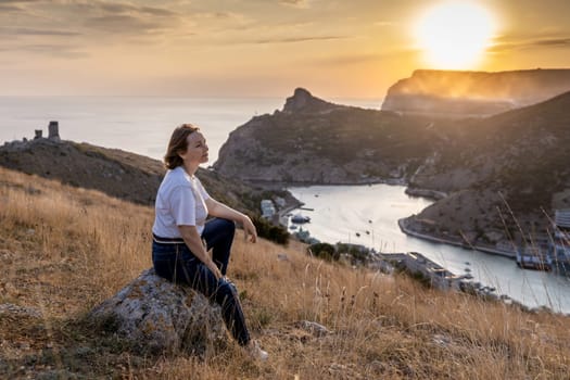 Happy woman on sunset in mountains. Woman siting with her back on the sunset in nature in summer. Silhouette