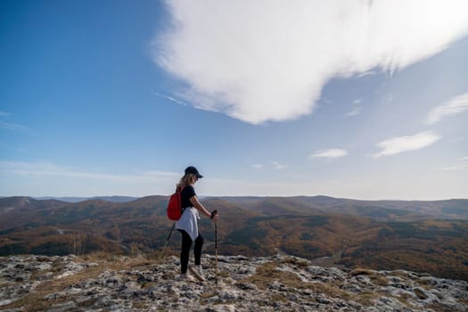 woman on mountain peak looking in beautiful mountain valley in autumn. Landscape with sporty young woman, blu sky in fall. Hiking. Nature.