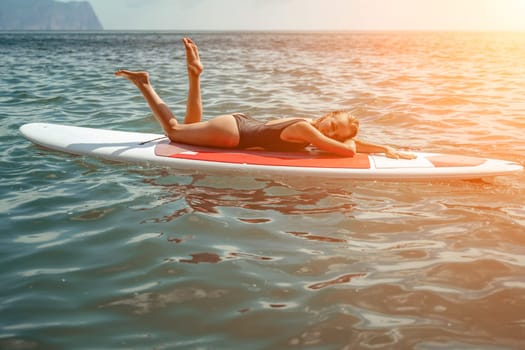 Woman sup sea. Sports girl on a surfboard in the sea on a sunny summer day. In a black bathing suit, he sits on a sapa in the sea. Rest on the sea