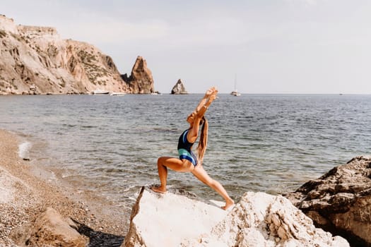 Yoga on the beach. A happy woman meditating in a yoga pose on the beach, surrounded by the ocean and rock mountains, promoting a healthy lifestyle outdoors in nature, and inspiring fitness concept