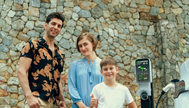 Family road trip vacation with electric vehicle, lovely family recharge EV car with green and clean energy. Stone seawall background and eco friendly car travel for sustainable environment. Perpetual