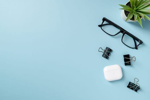 Top view of Glasses, black binder paper clip and headphones on blue table