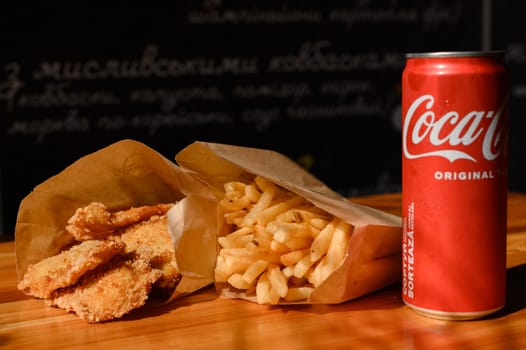 Ivano-Frankivsk, Ukraine March 26, 2023: Coca Cola and fried chicken nuggets, French fries on the table, a quick snack in a cafe.