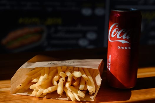 Ivano-Frankivsk, Ukraine March 26, 2023: Coca Cola and french fries in a paper bag on a black background.