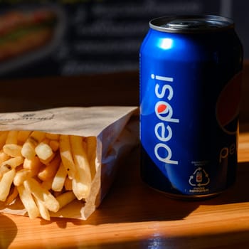 Ivano-Frankivsk, Ukraine March 26, 2023: Pepsi and french fries in a paper bag on a black background.