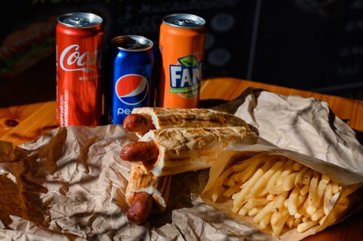 Ivano-Frankivsk, Ukraine March 26, 2023: three bottles of coke, fanta and pepsi with hotdogs and french fries on the table, fatty and unhealthy food.