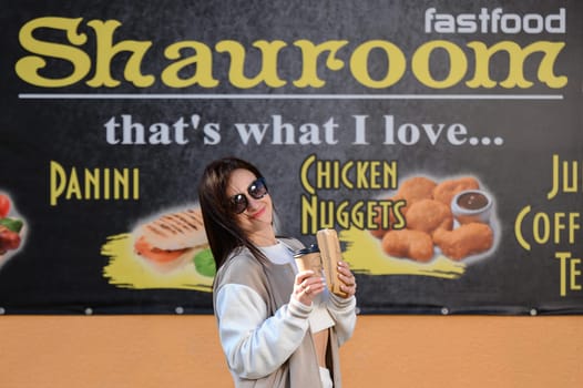 Ivano-Frankivsk, Ukraine March 26, 2023: a girl comes out of a cafe and holds coffee and shawarma in her hands, walking with food.