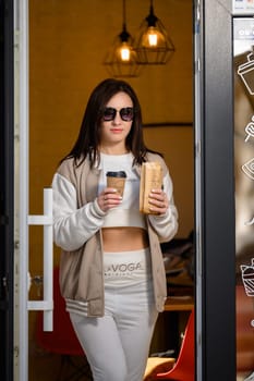 Ivano-Frankivsk, Ukraine March 26, 2023: a girl comes out of a cafe and holds coffee and shawarma in her hands, walking with food.