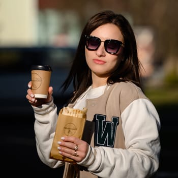 Ivano-Frankivsk, Ukraine March 26, 2023: Photo of a girl with shawarma and coffee on the street, a quick snack on the street.