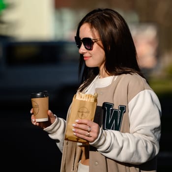 Ivano-Frankivsk, Ukraine March 26, 2023: Photo of a girl with shawarma and coffee on the street, a quick snack on the street.