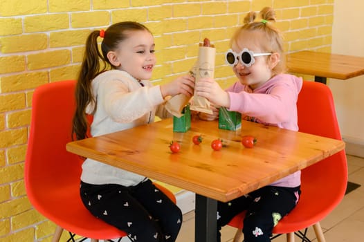 Ivano-Frankivsk, Ukraine March 26, 2023: Two little girls eat hotdogs in a cafe, junk food for children.