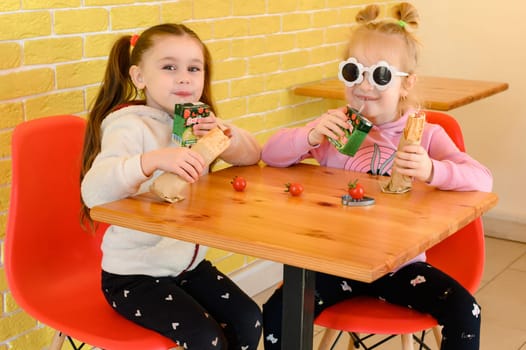 Ivano-Frankivsk, Ukraine March 26, 2023: two little girls in a cafe drinking juice and eating fries, children in a cafe.