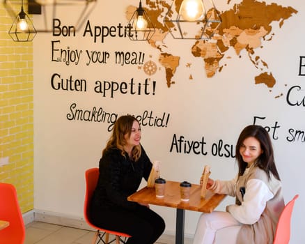 Ivano-Frankivsk, Ukraine March 26, 2023: two girls sit in a cafe and hold shawarma and coffee in their hands, a visit to the cafe