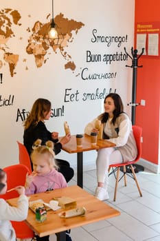 Ivano-Frankivsk, Ukraine March 26, 2023: two mothers and their daughters sit in a cafe and hold shawarma and coffee in their hands, a meeting of friends in a cafe.