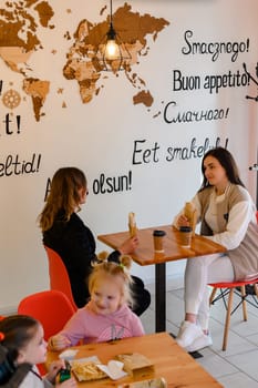 Ivano-Frankivsk, Ukraine March 26, 2023: two mothers and their daughters sit in a cafe and hold shawarma and coffee in their hands, a meeting of friends in a cafe.