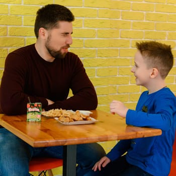 Ivano-Frankivsk, Ukraine March 26, 2023: A father and son eat chicken nuggets and French fries in a cafe.