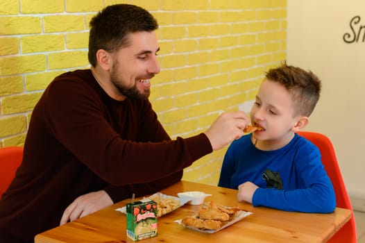 Ivano-Frankivsk, Ukraine March 26, 2023: A father and son eat chicken nuggets and French fries in a cafe.